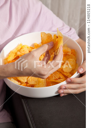 Caucasian person in pink t-shirt holding plate full of potato chips and preparing to eat 114805218