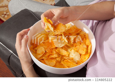 Caucasian person in pink t-shirt holding plate full of potato chips and preparing to eat 114805222