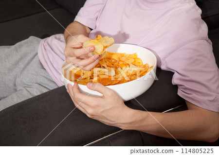 Caucasian person in pink t-shirt holding plate full of potato chips and preparing to eat 114805225