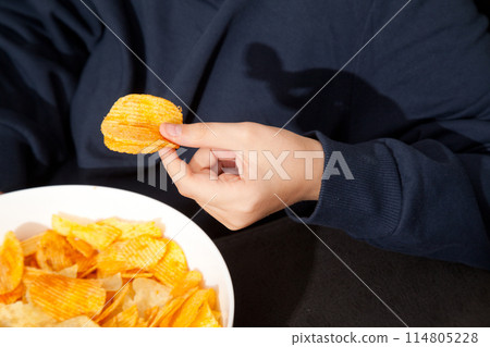 Caucasian person in navy blue t-shirt holding plate full of potato chips and preparing to eat 114805228