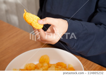 Caucasian person in navy blue t-shirt holding plate full of potato chips and preparing to eat 114805232