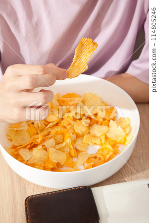 Caucasian person in pink t-shirt holding plate full of potato chips and preparing to eat 114805246
