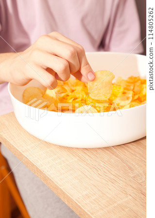 Caucasian person in pink t-shirt holding plate full of potato chips and preparing to eat 114805262