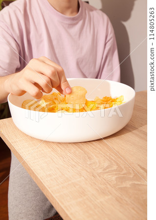 Caucasian person in pink t-shirt holding plate full of potato chips and preparing to eat 114805263