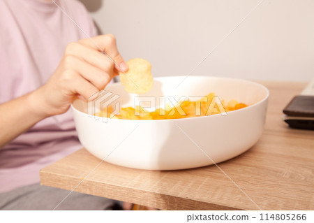 Caucasian person in pink t-shirt holding plate full of potato chips and preparing to eat Caucasian person in pink t-shirt holding plate full of potato chips and preparing to eat 114805266