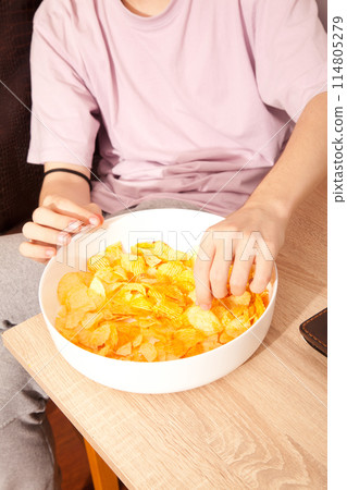 Caucasian person in pink t-shirt holding plate full of potato chips and preparing to eat 114805279