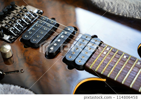 Electric guitar bridge, strings and pickup, detail close-up view of guitar pickup in wood walnut Electric guitar bridge, strings and pickup, detail close-up view of guitar pickup in wood walnut 114806458