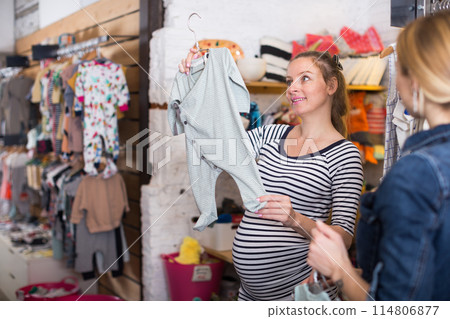 Pregnant woman in striped tunic communicates with seller in clothing store 114806877