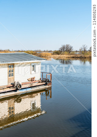 Floating house on calm river water under clear sky Floating house on calm river water under clear sky 114808293