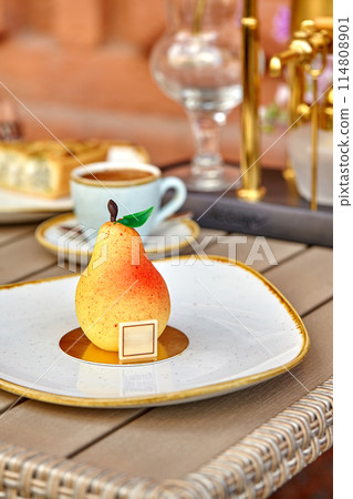 Speckled yellow and red pear-shaped dessert on plate in cafe 114808901