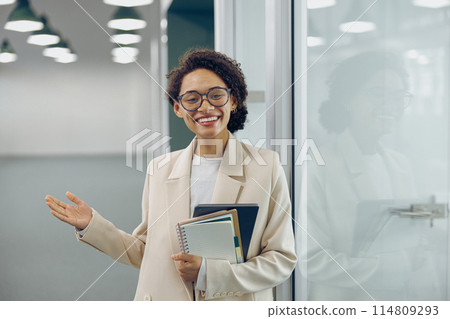 Smiling businesswoman in eyeglasses standing on modern coworking background and showing welcome sign 114809293