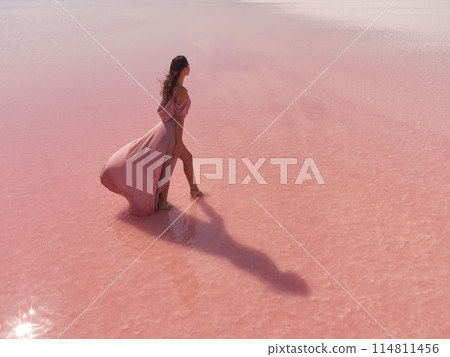 Fashionable Woman in Pink Long Dress in Water on Pink Salt Lake 114811456