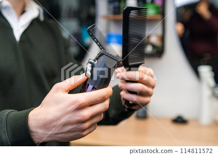 Barber holding combs and trimmer in the barbershop. Barber holding combs and trimmer in the barbershop. 114811572