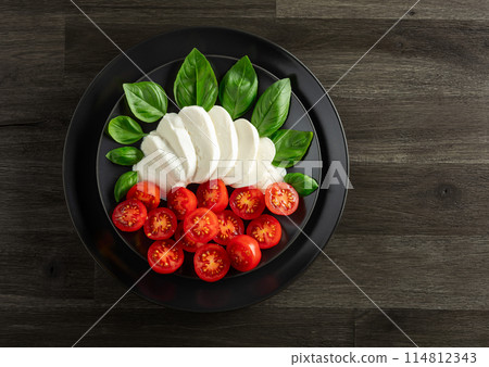 Mozzarella with basil and cherry tomatoes on an old wooden table. Mozzarella with basil and cherry tomatoes on an old wooden table. 114812343