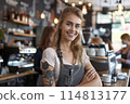 Radiant Tattooed Barista Smiles Warmly During a Bustling Morning Shift at a Cozy Coffee Shop 114813177
