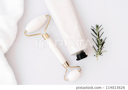Close up of white tube without label and facial roller on white marble table background. 114813626