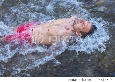 Man relaxing in mountain river. Healthy lifestyle. Calm man swimming in flowing water. Leisure activity. Beautiful man with closed eyes in waterfall. Breathtaking moment. Life balance.  114814302