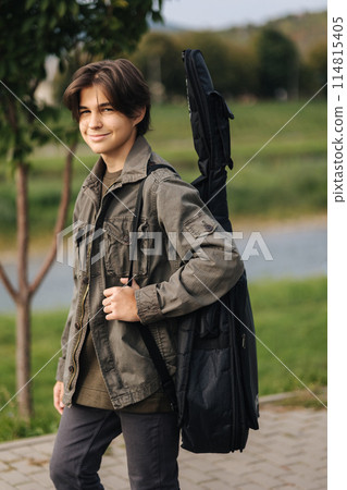 Teenage boy walking in the park with guitar on a case. Boy go to school of music 114815405