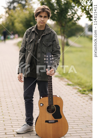 Concentrated teenage boy musician playing acoustic guitar outdoor. Handsome boy love music. Open your eyes. Focus on face 114815411