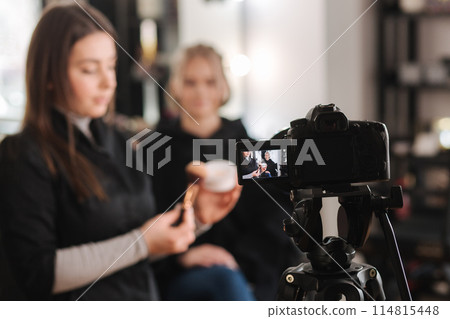 Woman making a video for her blog of making makeup, digital camera on tripod. Young female blogger on camera screen holding cosmetics 114815448