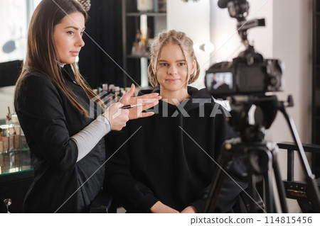 Woman making a video for her blog of making makeup, digital camera on tripod. Young female blogger on camera screen holding cosmetics Woman making a video for her blog of making makeup, digital camera on tripod. Young female blogger on camera screen holding cosmetics 114815456