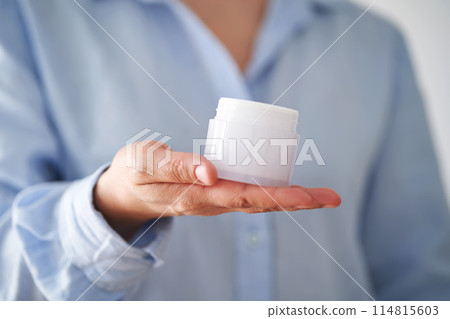 Hands in a blue shirt hold a jar of cream. 114815603