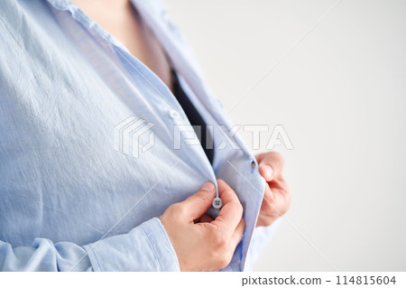 Women's hands button up a blue linen shirt. Women's hands button up a blue linen shirt. 114815604