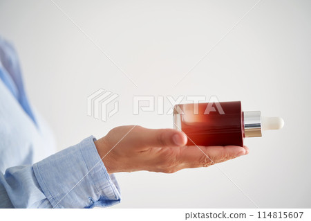 Female hands in a blue shirt hold a pink bottle of serum. 114815607