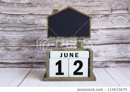 Chalkboard with June 12 date on white cube block on wooden table. 114815679