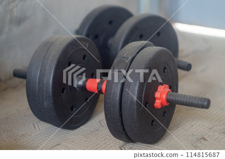 Pair Of Black Dumbbells On Gym Floor Near Concrete Wall In Daylight 114815687