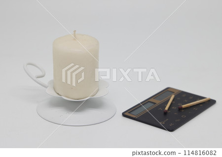 A candle in a white candlestick and matches on a calculator, is it worth it to burn. 114816082