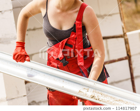 Woman carrying gutter on construction site 114817907