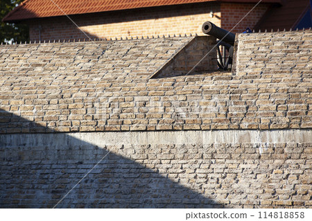 An ancient brick wall of the fortress. A large steel cannon on top of the wall. Background. Texture. Horizontal. An ancient brick wall of the fortress. A large steel cannon on top of the wall. Background. Texture. Horizontal. 114818858