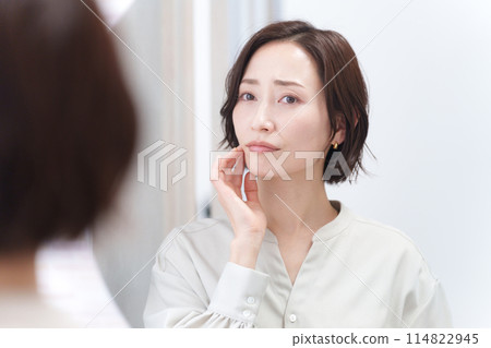 Middle-aged woman looking in the mirror and worrying about rough skin (beauty, skin care, skin troubles) 114822945