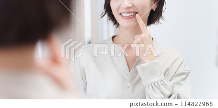 Middle-aged woman checking her teeth in the mirror (beauty, orthodontics, whitening) 114822968