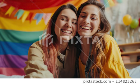 Happy lesbian couple on the background of a rainbow flag. PRIDE month and the LGBT+ movement. 114823265