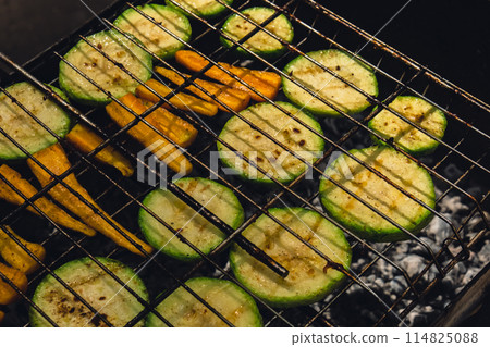 Chopped zucchini and carrots roasting on fire seasoned with aroma herbs and spices. Delicious fresh vegetables grilling on barbecue smoker grid. Diet vegan bbq. Outdoor recreation 114825088