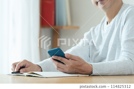 A middle-aged man checking his smartphone and notebook 114825312