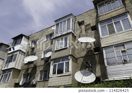 soviet five-storey apartment building with numerous windows and balcony and satellite dishes on the facade at summer day soviet five-storey apartment building with numerous windows and balcony and satellite dishes on the facade at summer day 114826425