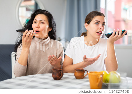 Two smiling women using phones at home 114827408