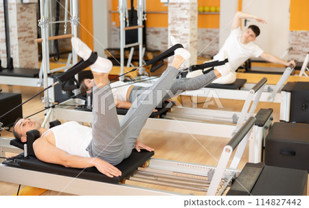 Man works out in gym and performs set of exercises to stretch leg muscles with help of reformer Man works out in gym and performs set of exercises to stretch leg muscles with help of reformer 114827442