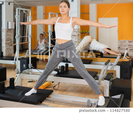 Girl stands on reformer and performs exercises to balance Girl stands on reformer and performs exercises to balance 114827580