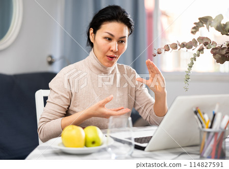 Woman sitting at table at home and having video call conversation 114827591