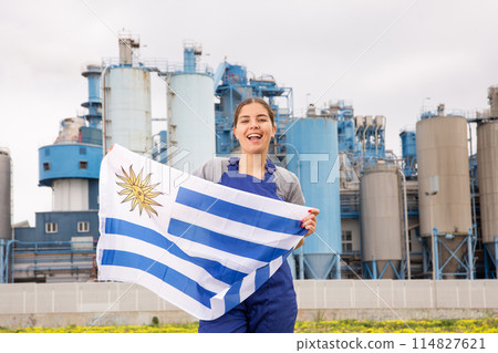 Cheerful young woman in workwear holds the national flag of Uruguay 114827621