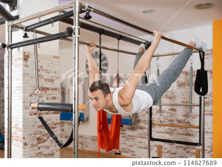 Man performing hanging back lever on Pilates trapeze table 114827689