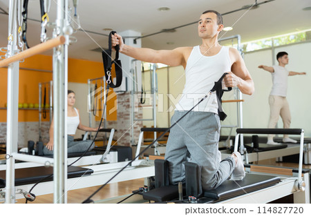 Man performing pulling straps exercise on Pilates reformer Man performing pulling straps exercise on Pilates reformer 114827720
