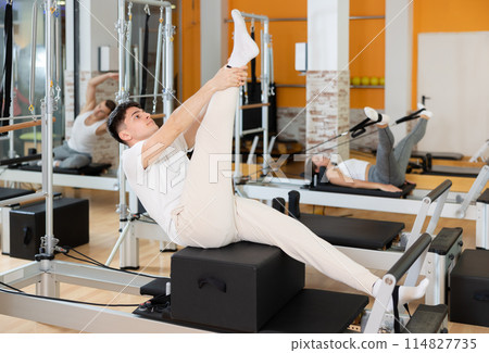 Guy performing exercises on Pilates reformer with sitting box Guy performing exercises on Pilates reformer with sitting box 114827735