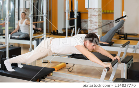 Man in different poses performs static and dynamic exercises on reformer Man in different poses performs static and dynamic exercises on reformer 114827770
