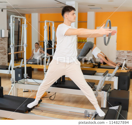 Guy performing pilates exercises with resistance ring on reformer Guy performing pilates exercises with resistance ring on reformer 114827894
