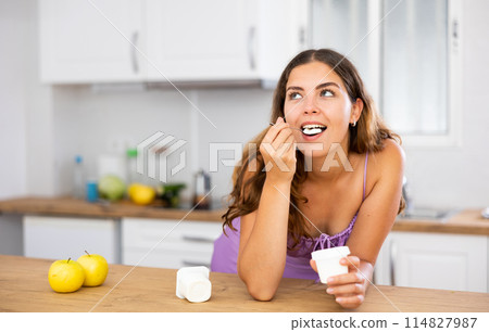 Portrait of young woman eating yoghurt at home 114827987